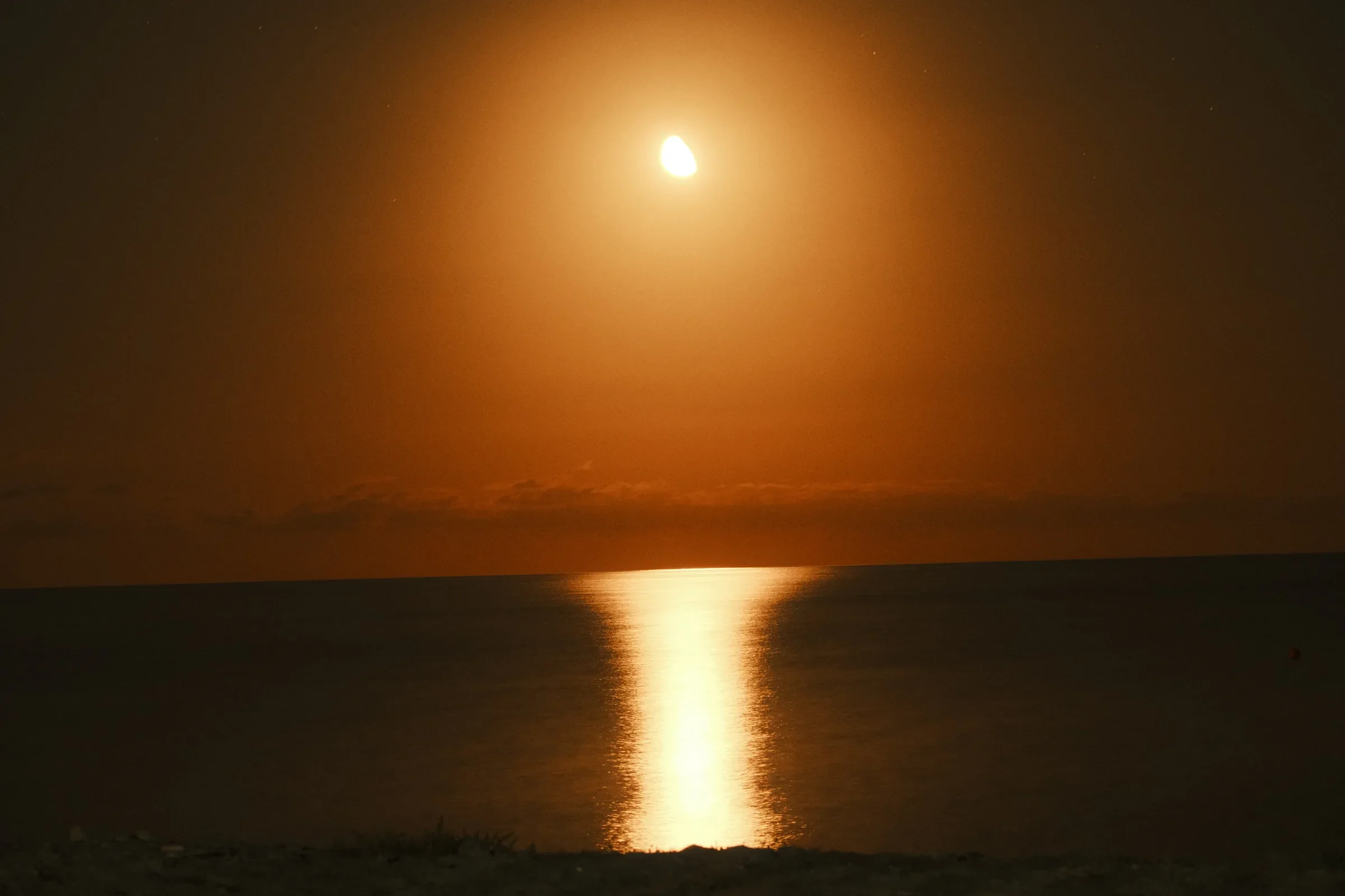 An amber moon above the sea with a narrow golden reflection